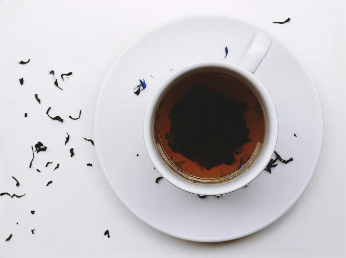 Black tea in a white cup with loose tea leaves